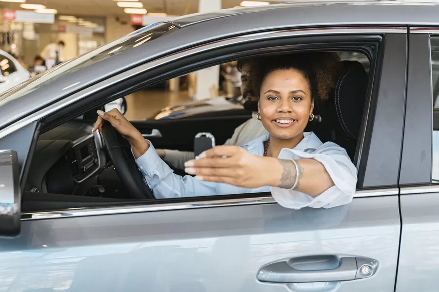 A new owner smiling behind the wheel of her car, holding up the key